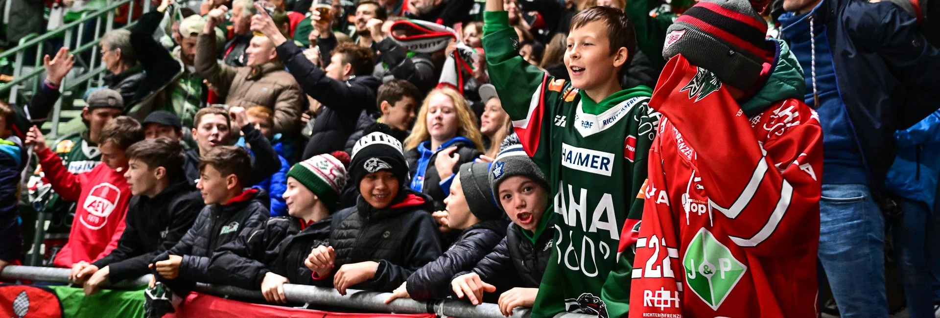 Man sieht einige Kinder in der ersten Reihe im Fanblock stehen.