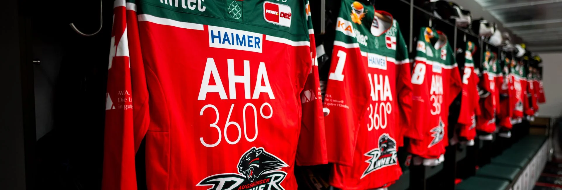 Man sieht einige AEV-Trikots aufgehängt. Der Bild-Fokus steht auf dem Sponsor "AHA 360°"