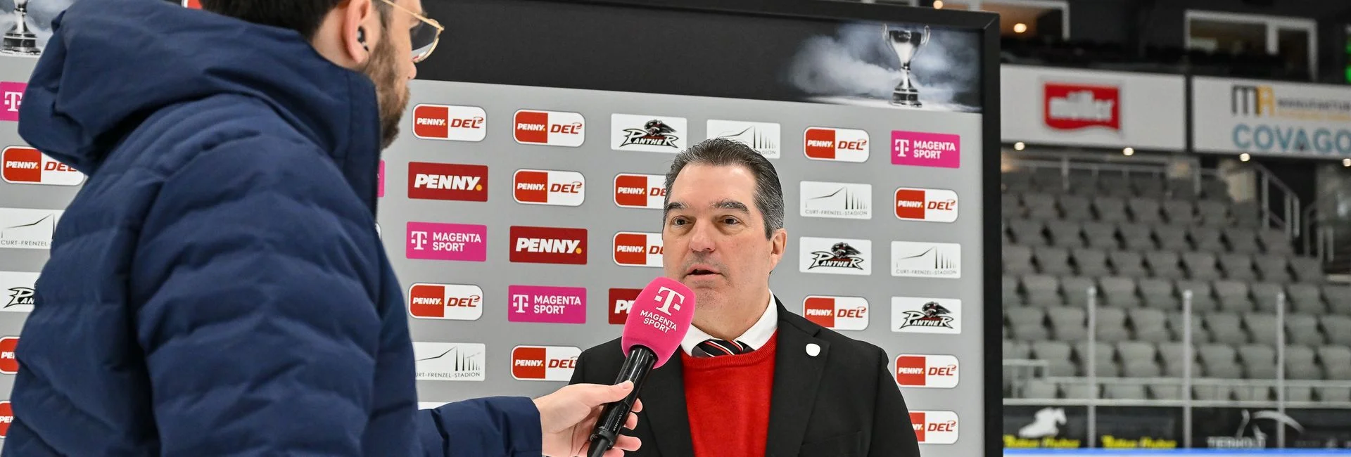 Man sieht Larry Mitchell beim Interview vor der Sponsorenwand. Das Interview führt ein Redakteur von Magenta Sport